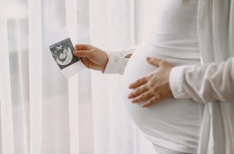 Woman standing by the window. Pregnant looking at photo. Woman expecting a baby.
